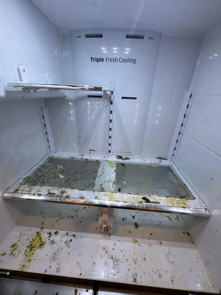 The same refrigerator before cleaning, with spilled food across every shelf
